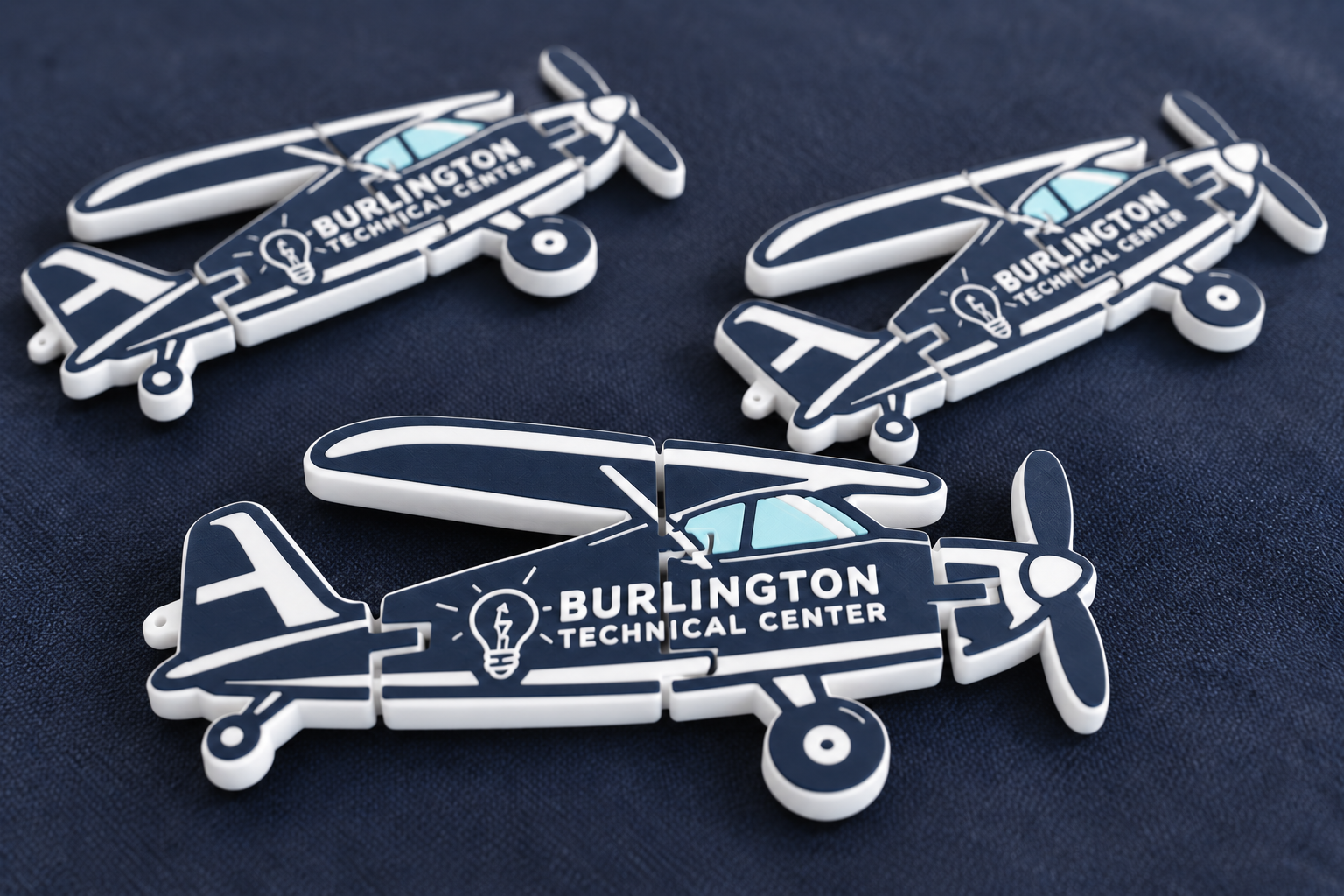 Close-up of Burlington Technical Center 3D-printed aircraft keychains on navy fabric